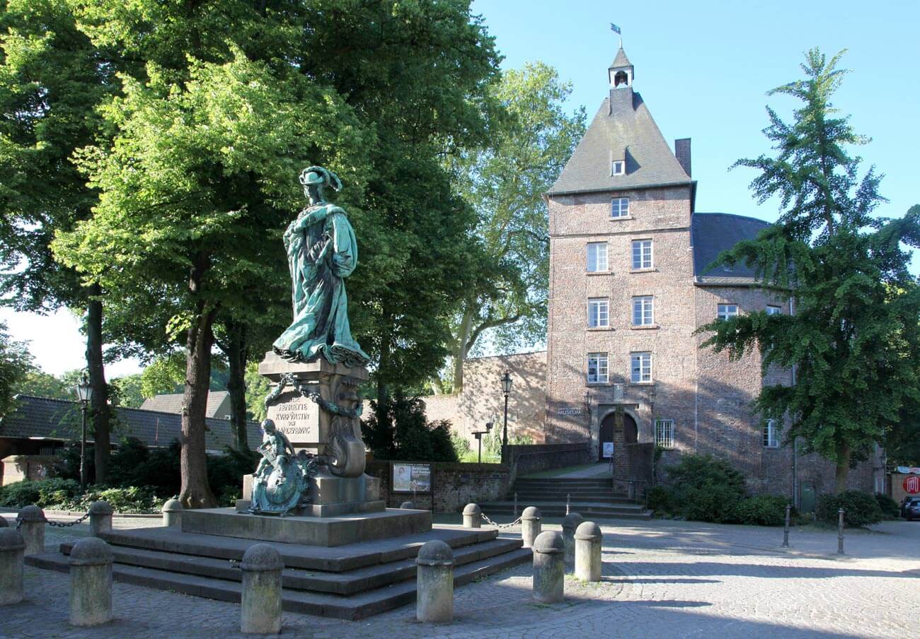 as Foto zeigt das Moerser Schloss mit dem Grafschafter Museum. Vor dem Schloss steht die Statue von Luise Henriette von Oranien. 