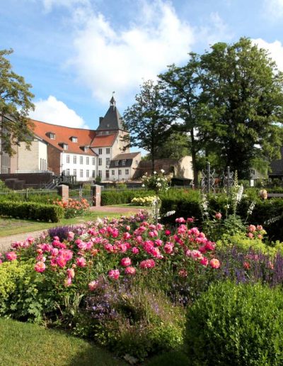 Das Foto zeigt den Rosengarten am Moerser Schloss. Direkt dahinter liegt der Schlosspark mit seinem historischen Baumbestand.